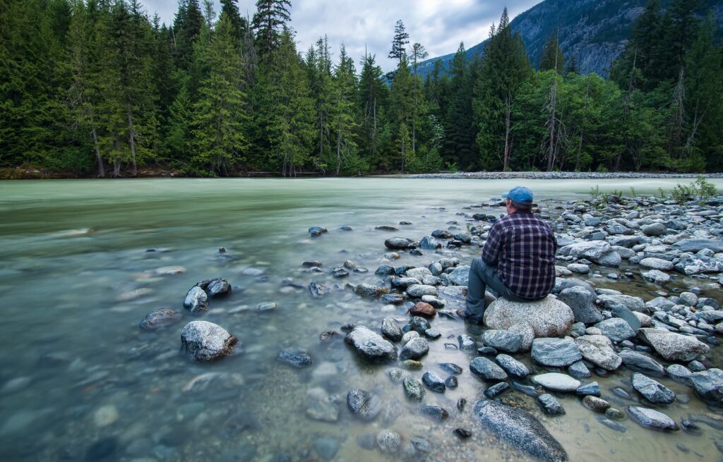 photo of man sitting by river, depicting making choices for ourselves to help us make up for lost time.