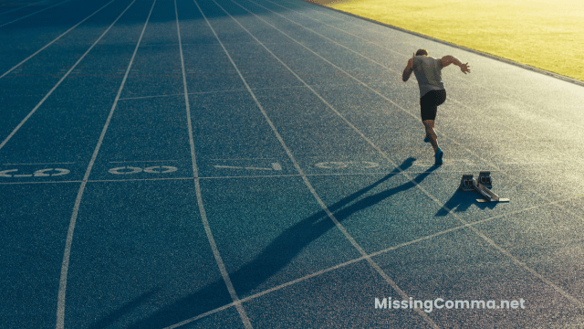 view from behind runner taking off from blocks on running track. Morning sunlight showing from the right