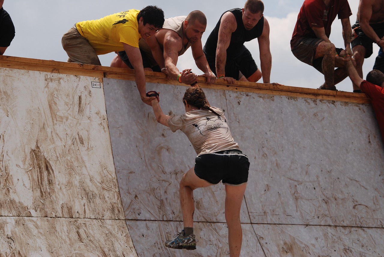 people helping competitor up a mud slicked wall